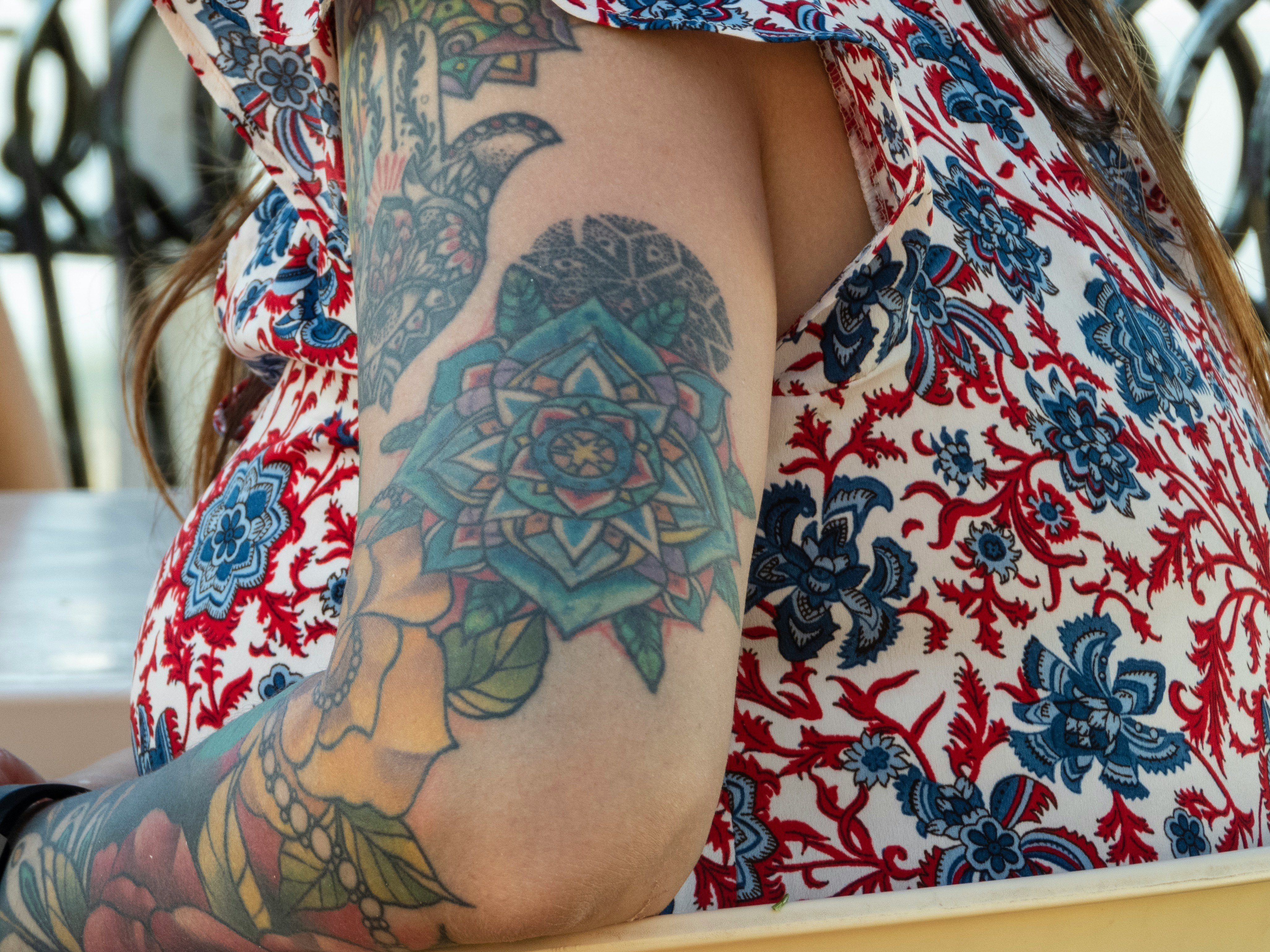 woman wearing red, blue, and white floral top with multicolored flower arm tattoo